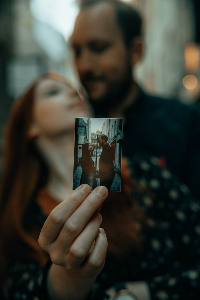 Мужчина обнимает женщину, держащую в руке печатную фотографию, на которой изображены они сами.