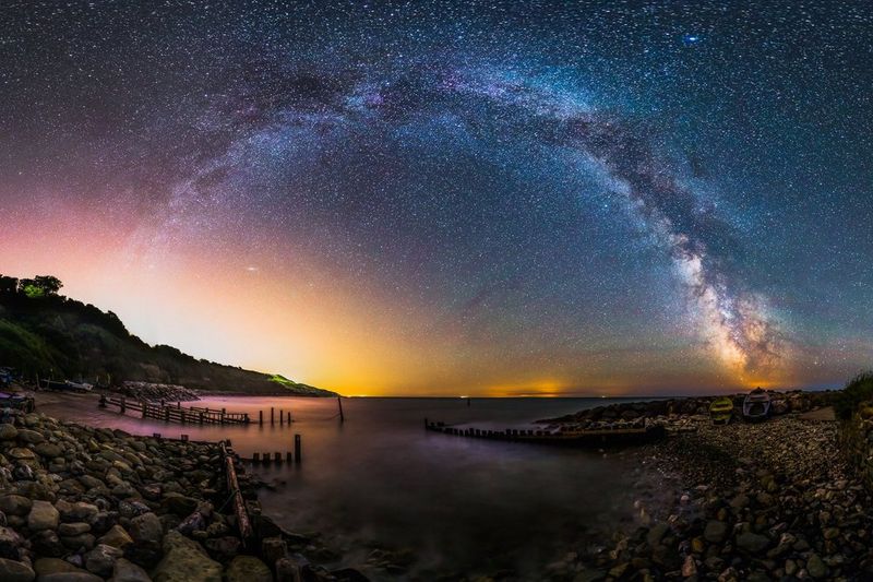 The Milky Way arcs across the sky above the rocky shores of a lake.