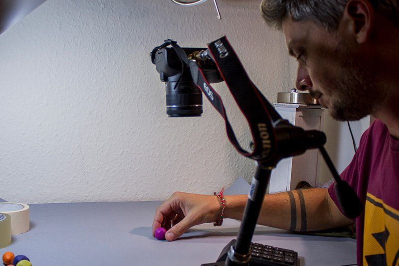 Ed Jackson, by his camera on a tripod and a desk lamp, adjusting a ball of pink clay.