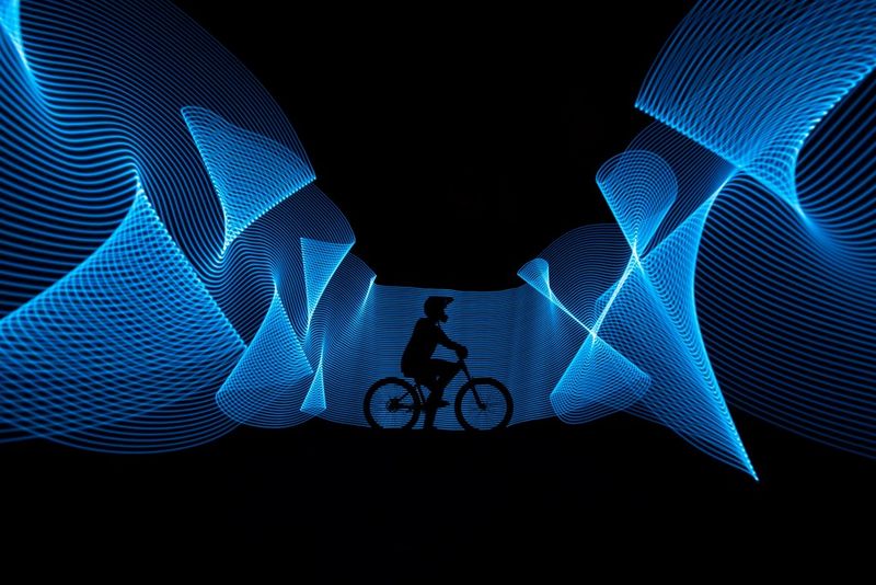 Eine schwarze Silhouette einer Person auf einem Fahrrad, umgeben von blauen Lichtspuren