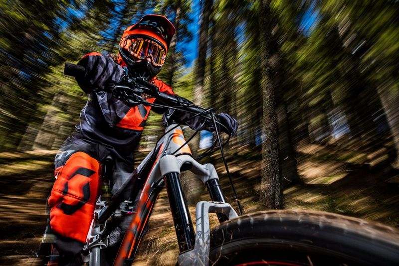 Eine orange-schwarz gekleidete Person fährt auf einem Mountainbike, während der Wald um sie herum verschwimmt.