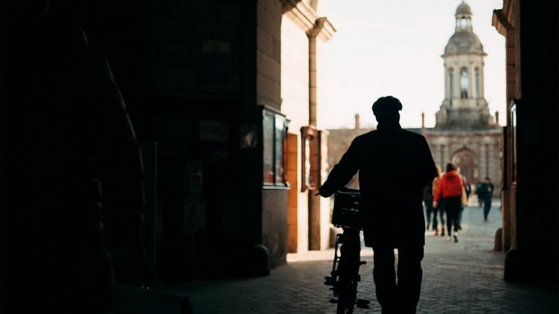 A man walking with his bike through an archway. 