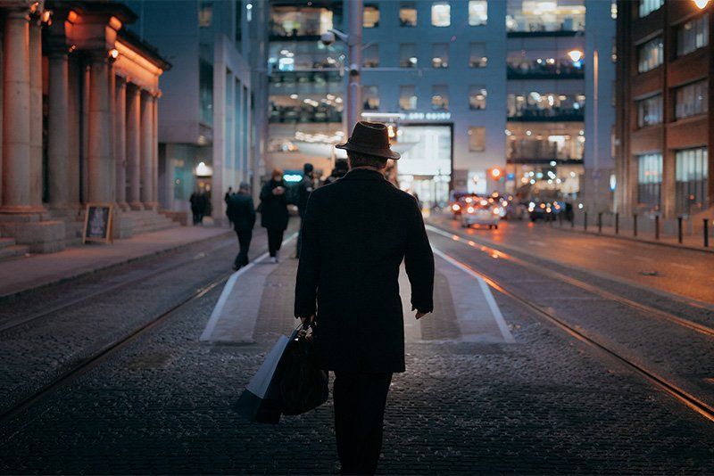A man in a hat walking to the tram platform in Dublin at night.