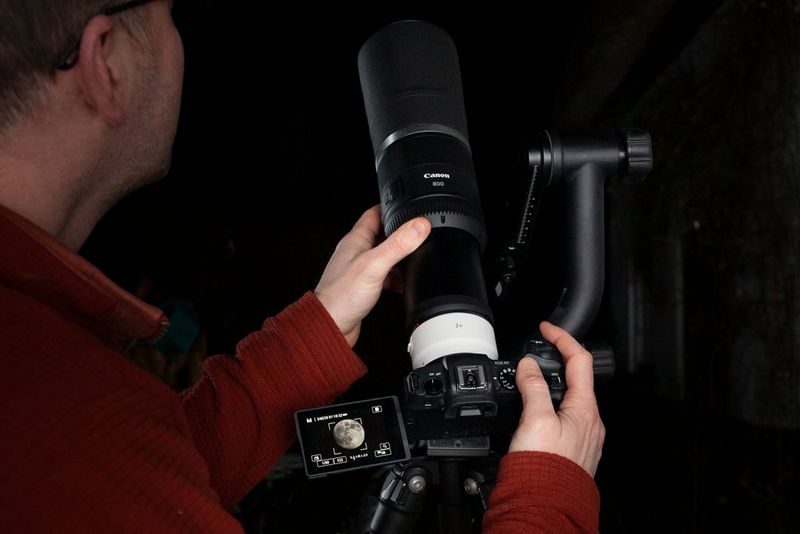 A photographer adjusting his Canon RF 800mm F11 IS STM lens on an EOS RP camera on a tripod.
