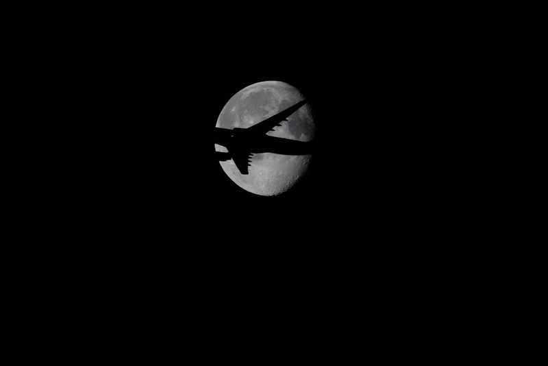 An aircraft silhouetted as it flies in front of a full moon.