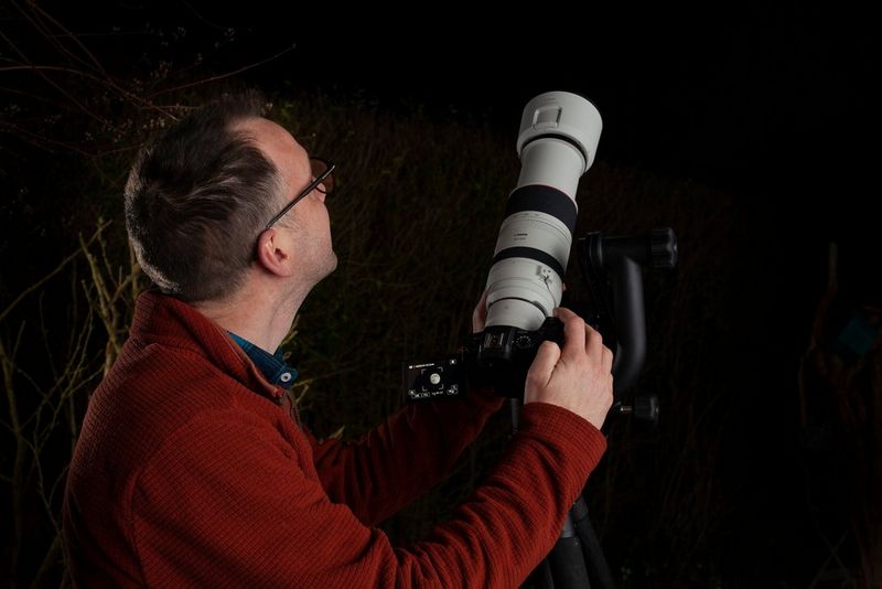 A photographer adjusting his EOS RP camera with an RF 100-500mm F4.5-7.1 L IS USM lens on a tripod.