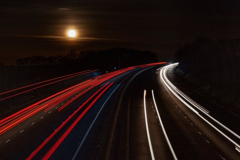 A moonscape over a motorway with traffic trails caused by a long exposure.