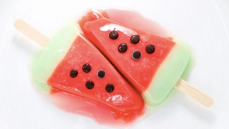 Two ice creams designed to look like slices of watermelon, starting to melt on a plate.