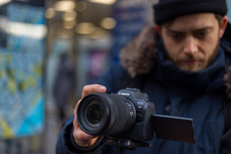 Muž v kabátu a vlněné čepici upravuje nastavení fotoaparátu Canon EOS R6 na stativu.