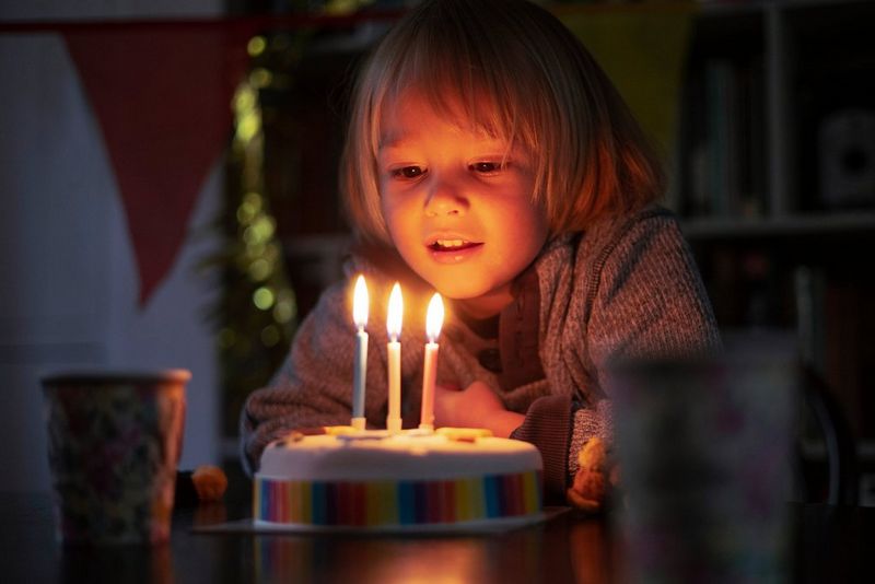 ילד קטן רוכן קדימה כדי לכבות את הנרות של עוגת יום הולדת. הפנים של הילד מוארים על-ידי הלהבות..