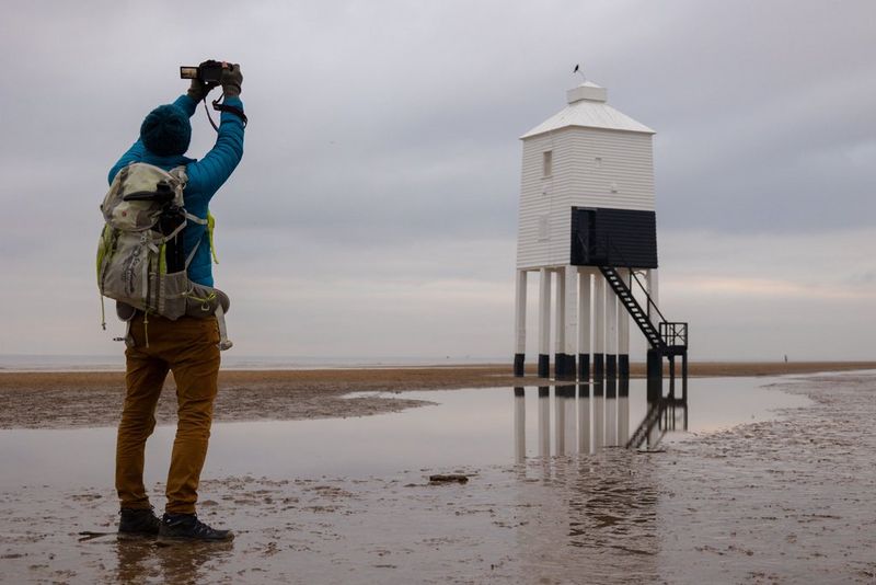 Un homme tenant son appareil photo au-dessus de sa tête pour photographier un avant-poste sur une plage.
