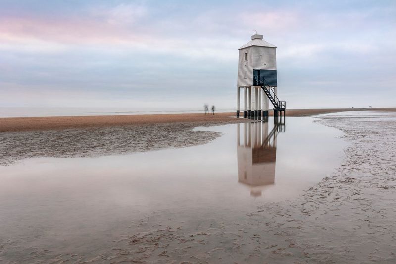 Photo d'un paysage de plage avec un avant-poste qui se reflète dans l'eau sur le sable.