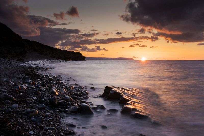 Une exposition longue de la mer qui se brise sur les rochers d'un rivage au coucher du soleil.