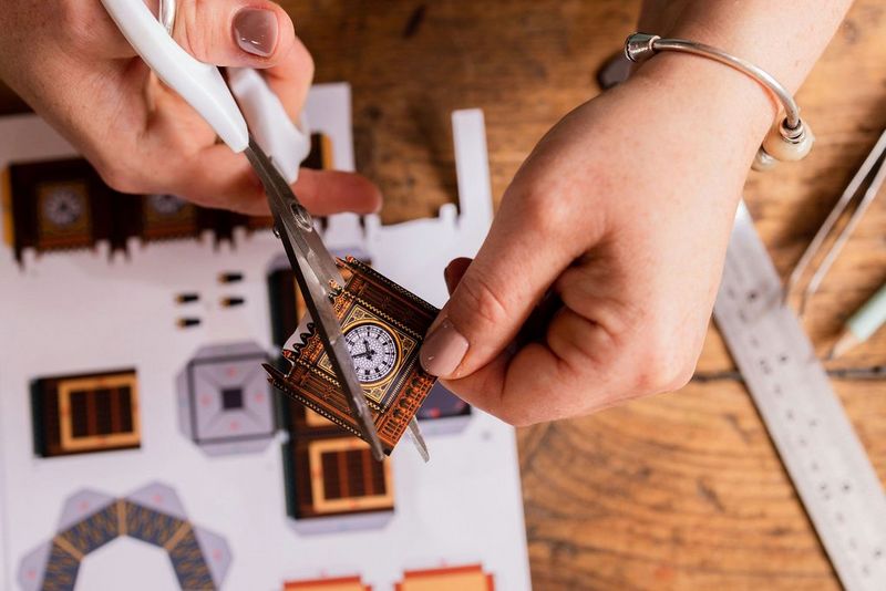 Handen die met een schaar delen uitknippen uit een Canon Creative Park-sjabloon van de Big Ben, geprint op Canon matglans fotopapier.