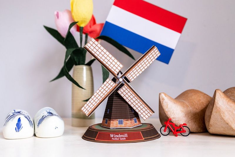 Een papieren windmolen gemaakt van een Creative Park-sjabloon die is uitgestald naast een vlag van Nederland, een fietsje en een paar houten klompen.