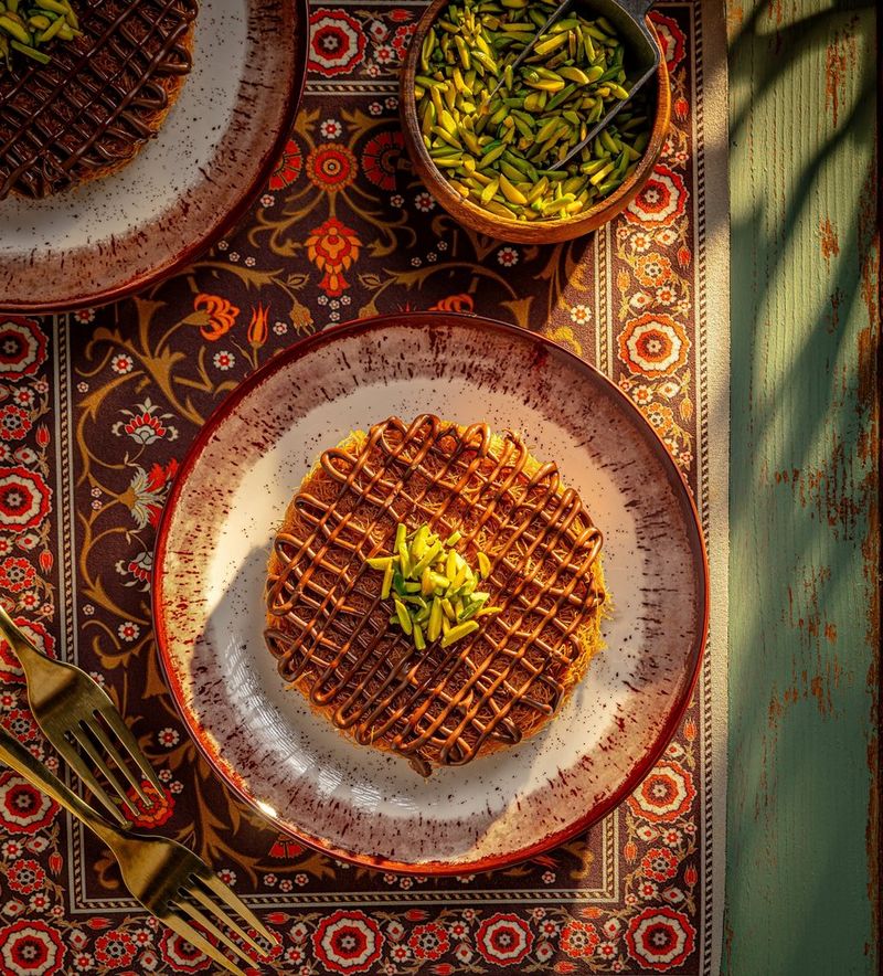 Twee borden met künefe met chocoladesaus, gegarneerd met een paar pistachenootjes.