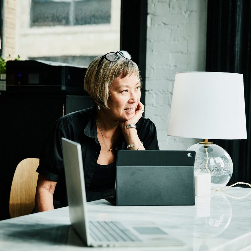 Woman sits with her iPad on a marble table, looking out the window