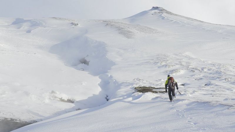 A lone figure walks through a snow-covered landscape towards a distant hill, in a well-exposed still from an HDR video.
