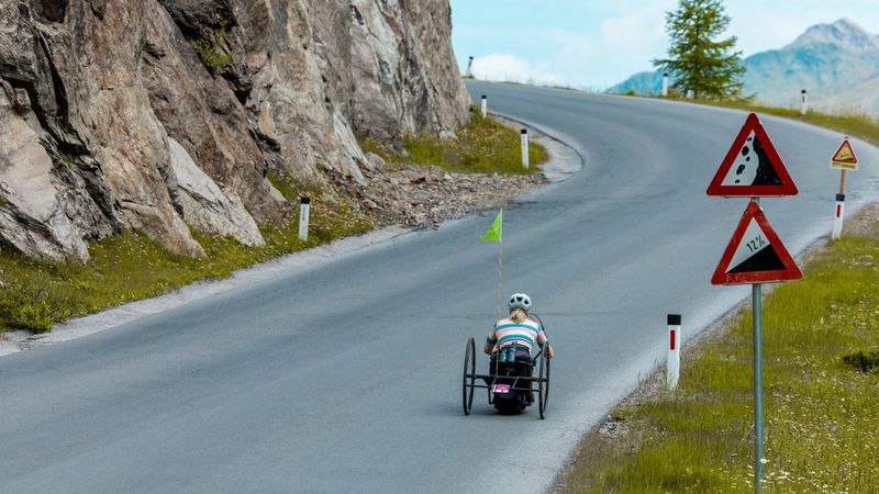 A person in a handbike is riding up a steep, winding mountain road.