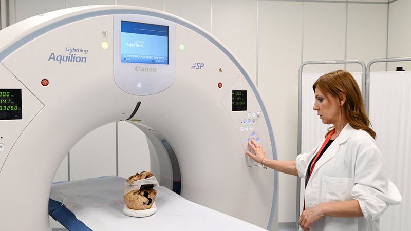 Una tecnica in camice bianco aziona uno scanner Canon Medical Aquilion Lightning SP. Un cranio antico è posizionato sul tavolo d'esame.