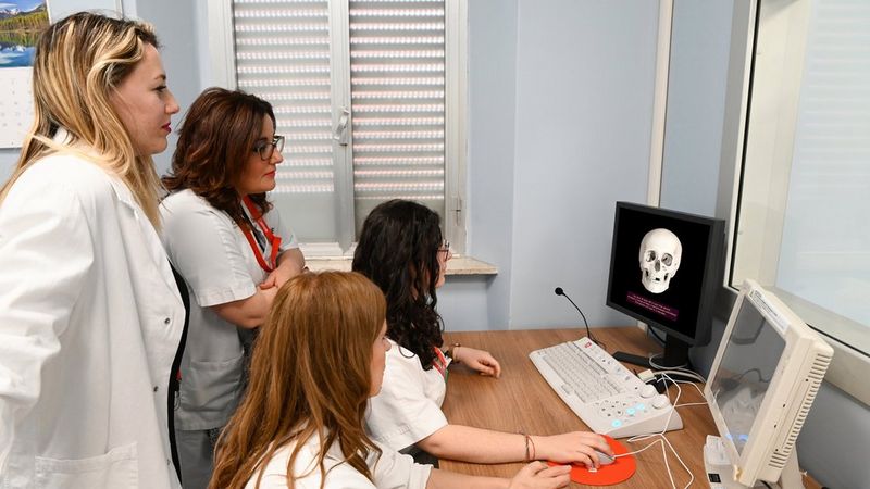 Quattro professionisti in camice osservano uno schermo che mostra una ricostruzione digitale 3D di un cranio umano.