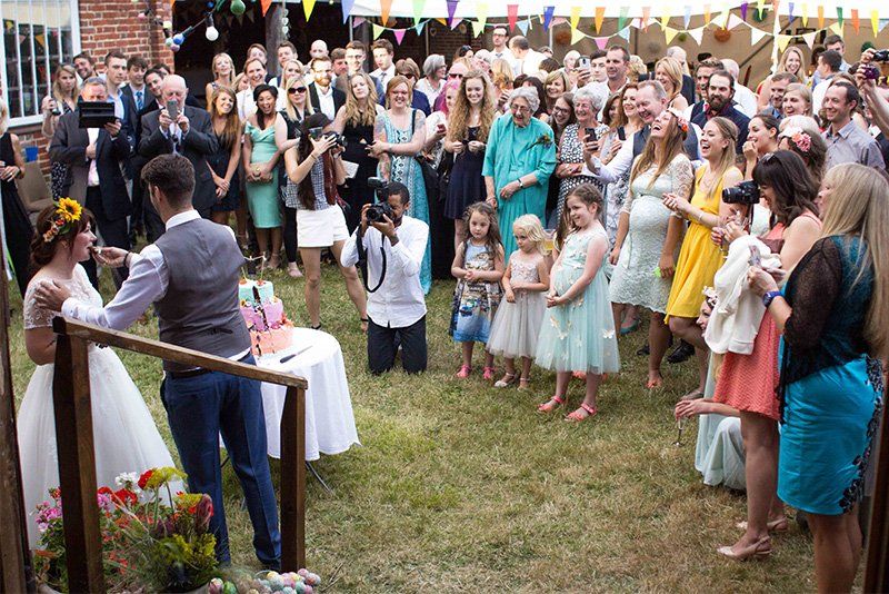 Wedding guests gather around the bride and groom as they cut the cake.