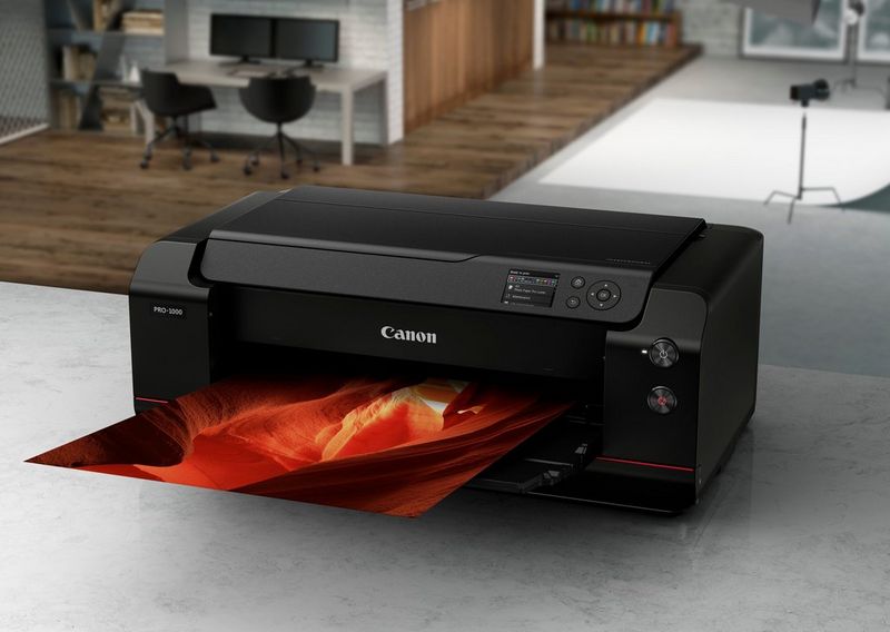 A Canon imagePROGRAF PRO-1000 printer and Canon camera on a glass table surrounded by prints.
