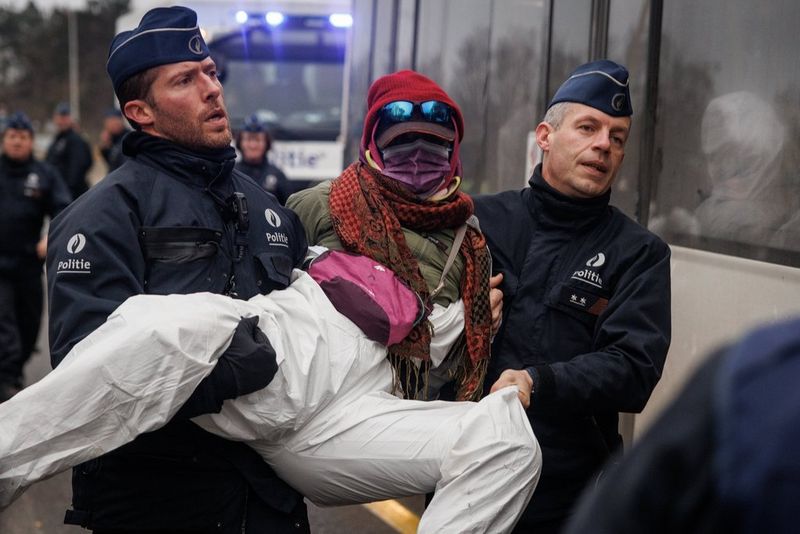 A person, face concealed, being carried by two police officers. Shot on Canon.