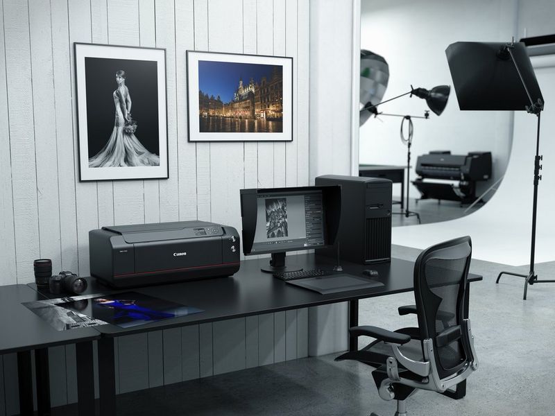 Una scrivania in uno studio fotografico professionale con un computer, un monitor, una fotocamera Canon e una stampante Canon imagePROGRAF PRO-1100.