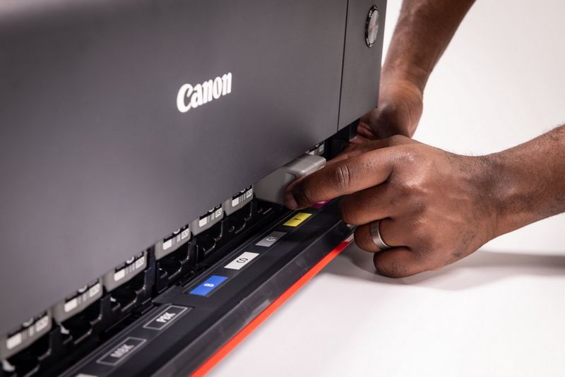 De hand van een gebruiker vervangt een van de 12 inktcartridges aan de voorkant van een Canon imagePROGRAF PRO-1100-printer.