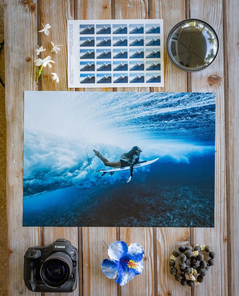A print of a surfer produced on the imagePROGRAF PRO-1100 printer sits on a wooden table, with a Canon EOS R1 camera below and a hard proof with colour thumbnails above.
