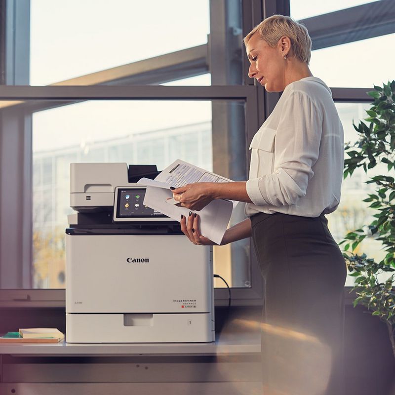 En kvinde står og kigger på et udprint fra en Canon office maskine.