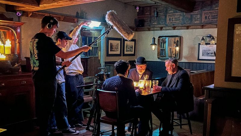 Student camera crew filming three actors sitting having a drink in an old-fashioned pub