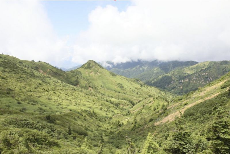 A view of a valley with green hills and fluffy clouds in the sky above.