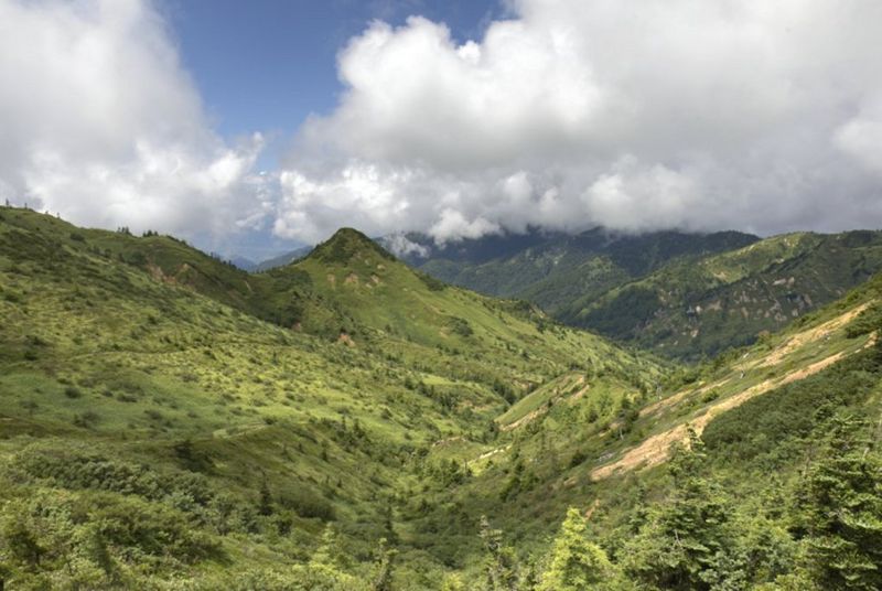 A view of a valley with green hills and fluffy clouds in the sky, with more detail and richer colours.