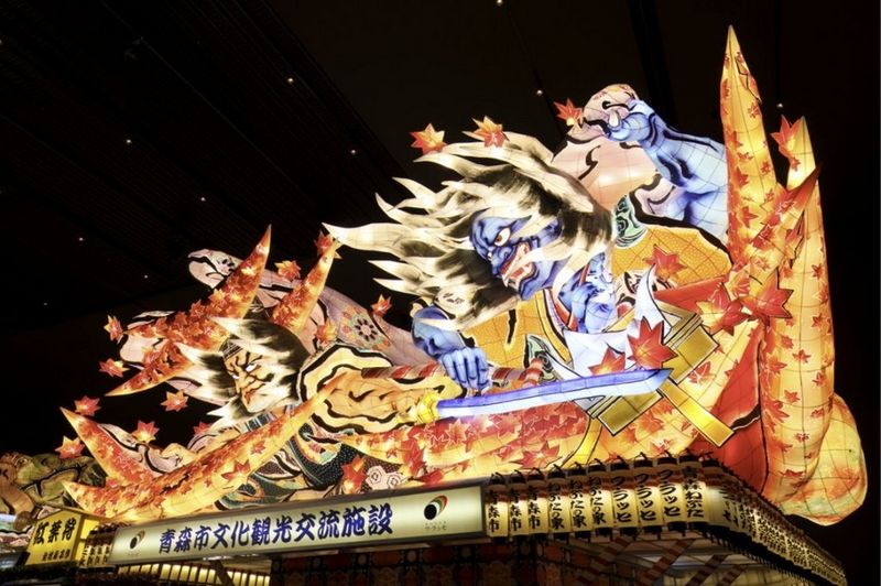 A brightly-lit display of manga characters, with rich yellow, orange and red colours against a night sky.