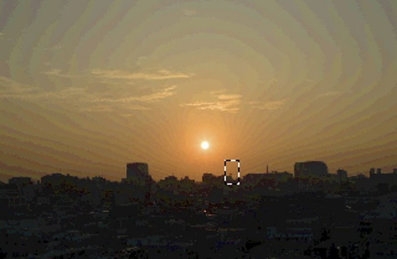 The same shot of the sunrise over a city lightened, with prominent banding in the sky.
