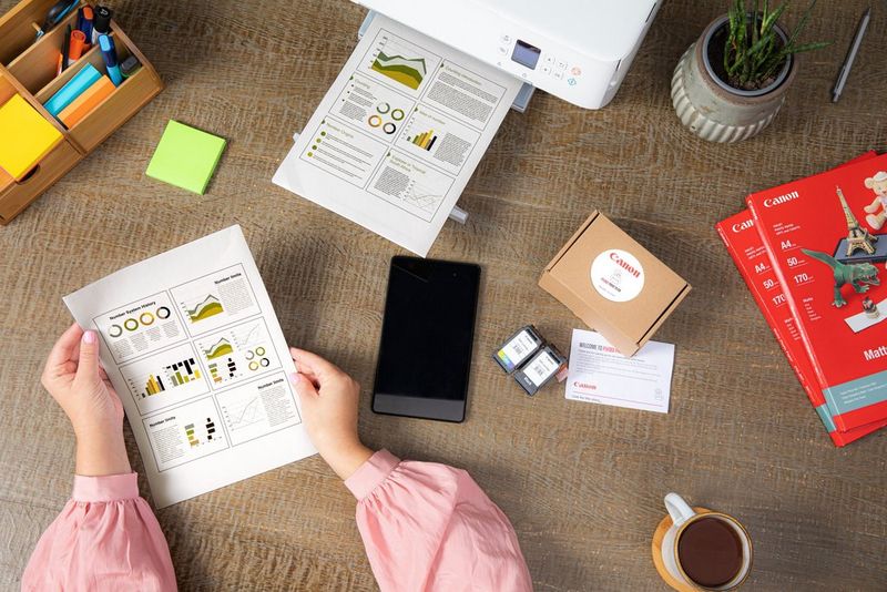 Et par hænder holder et print med grafik på, og en anden side kommer frem fra en Canon-printer.