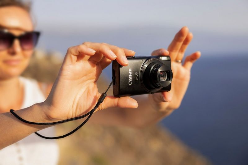 Женщина делает фото пляжного пейзажа на черную камеру Canon IXUS 285HS A.