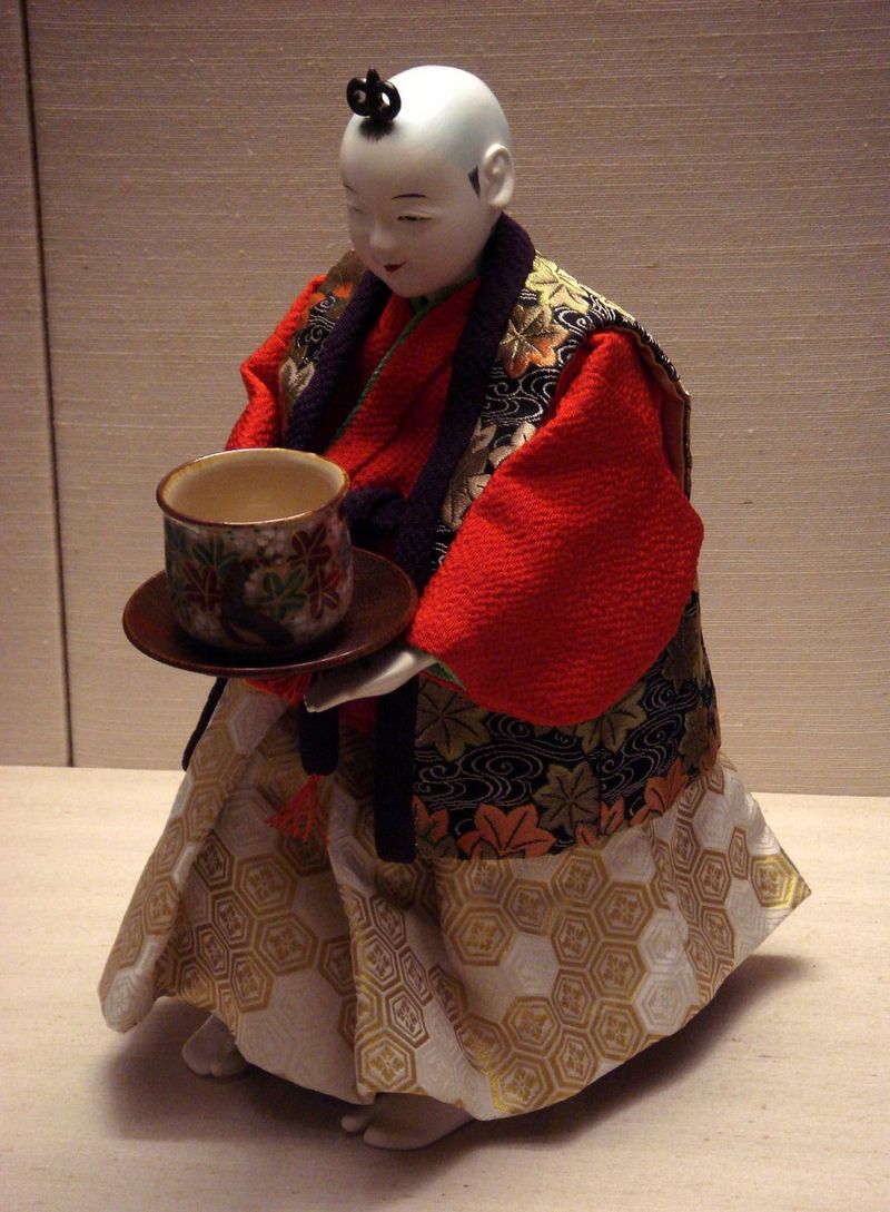 A porcelain-skinned Japanese doll in patterned dress, holding a teacup.