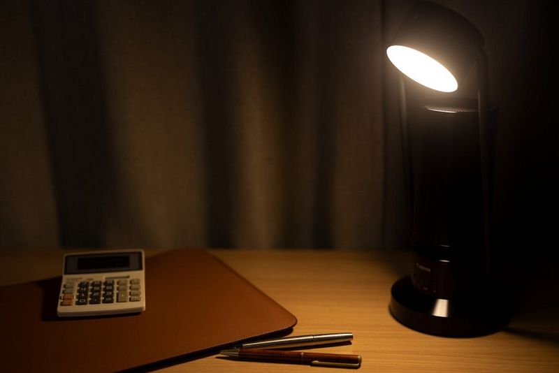 Een Canon Speakerlamp ML-A is op een bureau geplaatst en schijnt licht op een rekenmachine en enkele pennen.