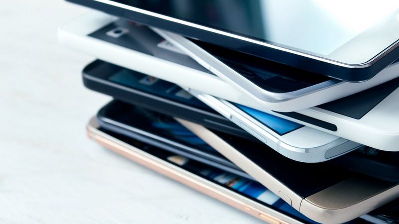 A stack of eight smartphones, viewed from the side, of different styles and colours.