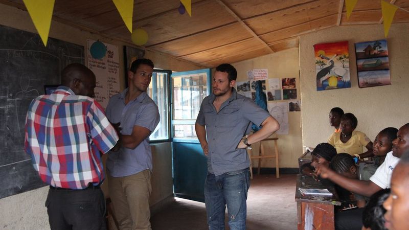 Three men stand by the blackboard of a classroom, as the students watch them.