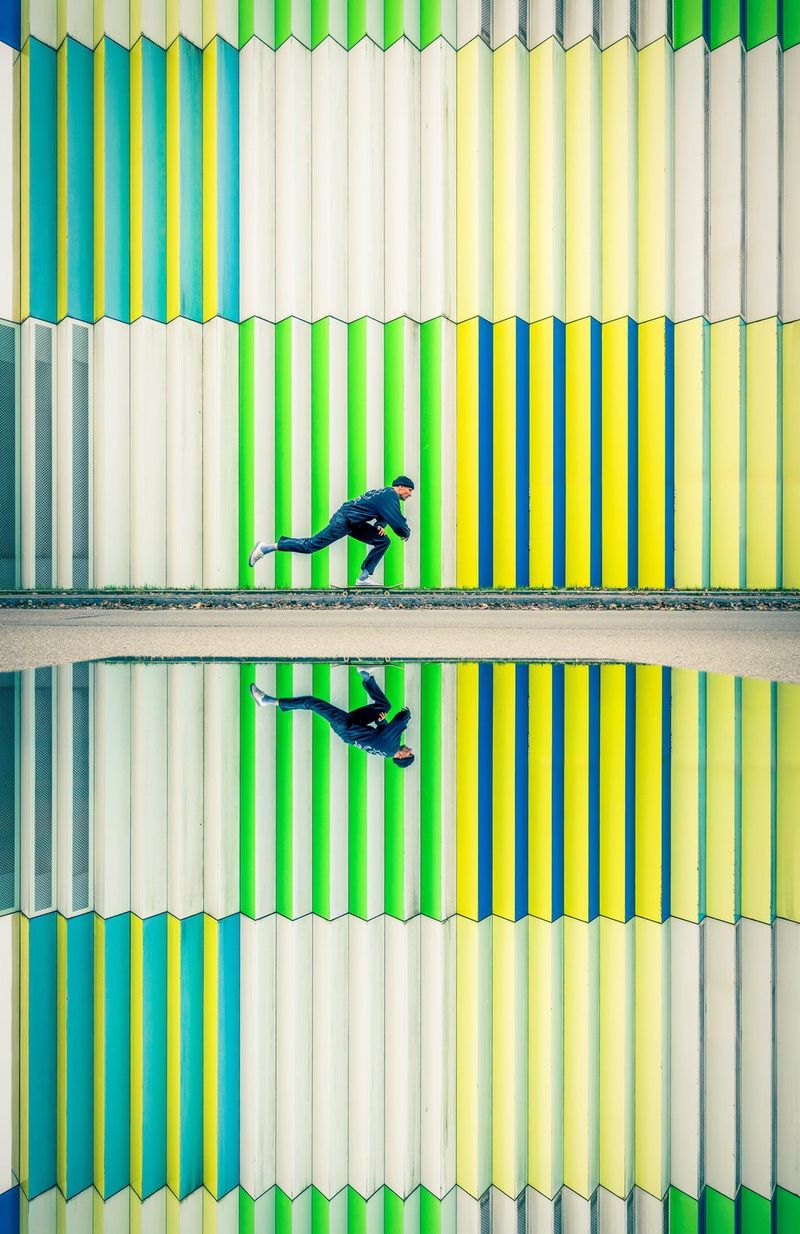 A skateboarder speeds past a colourful wall, his image reflected in a mirror in the foreground. Action photo taken on a Canon EOS R5 Mark II with a Canon RF 15-35mm F2.8L USM lens.