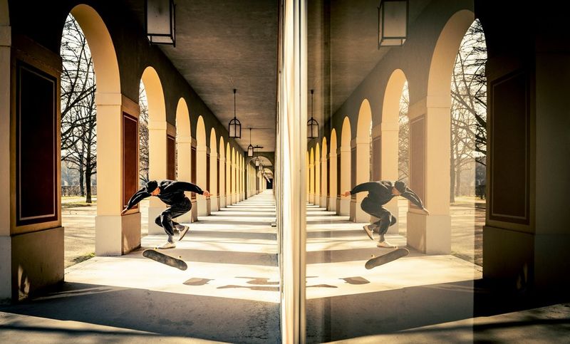 An action photo showing a skateboarder performing a trick in an arched colonnade, with the scene also reflected on the other side of the frame. Taken on a Canon EOS R5 Mark II with a Canon RF 15-35mm F2.8L USM lens.