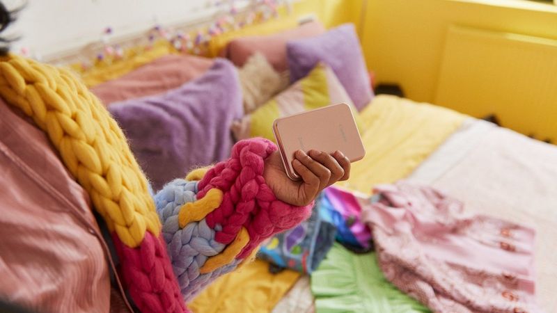 The arm of someone wearing a colourful cardigan. In their hand is a rose gold coloured Canon Zoemini pocket-sized printer.