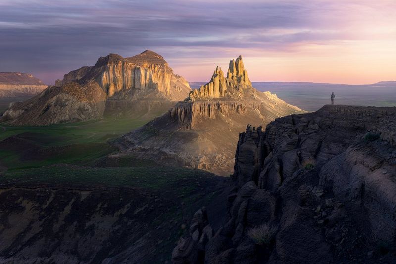 Een groothoek-landschapsfoto van een bergketen bij zonsondergang, met op de voorgrond een persoon die aan de rand van een klif staat. Foto gemaakt door Luka Vunduk met de Canon