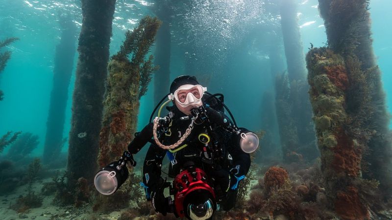 Marcia, aan het duiken met professionele onderwatercamera-apparatuur en verlichting, omringd door grote onderwaterplanten.