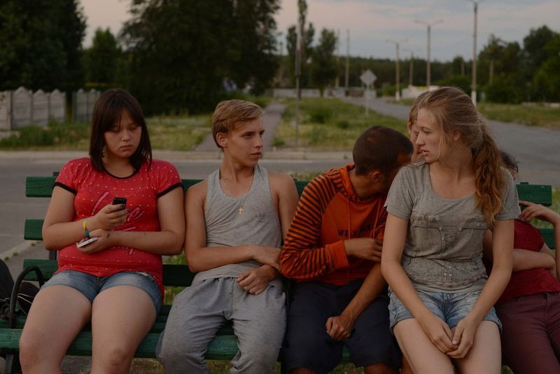 Six teenagers from Shchastia in Donbass, Ukraine, sit on a bench together, an image captured by Marion Pehee.