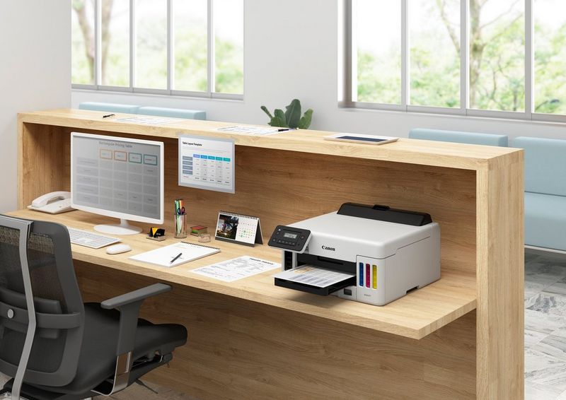 De MAXIFY GX5050-printer op een overzichtelijk bureau met kantoorbenodigdheden, een monitor, een toetsenbord en een telefoon.